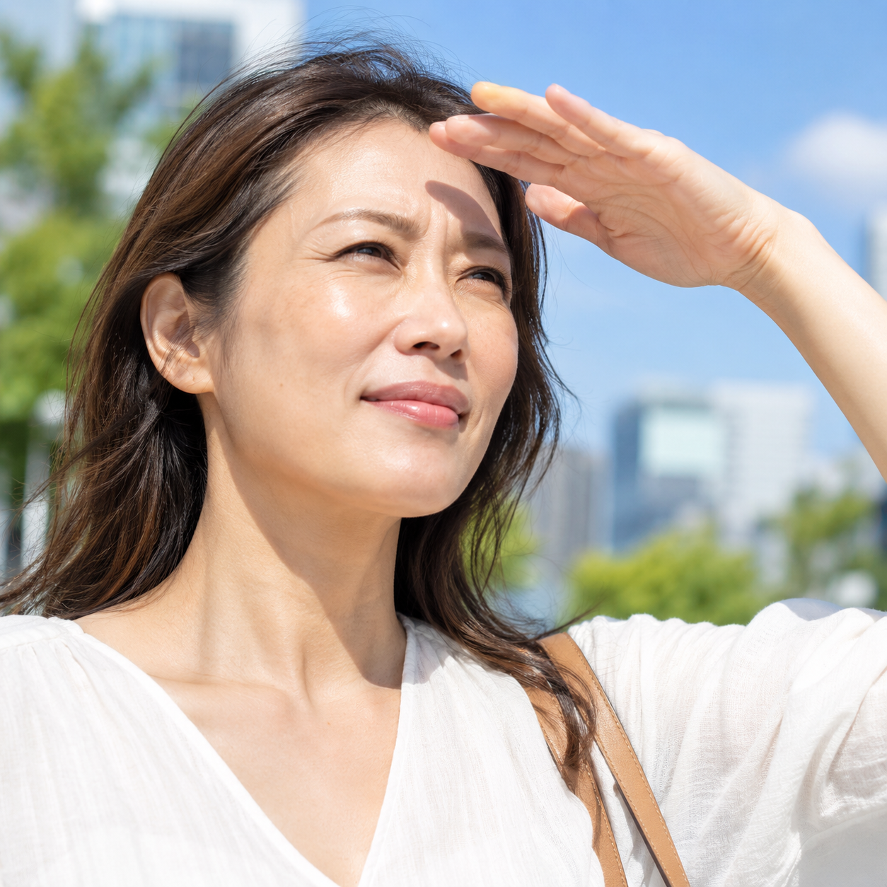 Asian woman squinting and shielding her eyes from bright sunlight outdoors.
