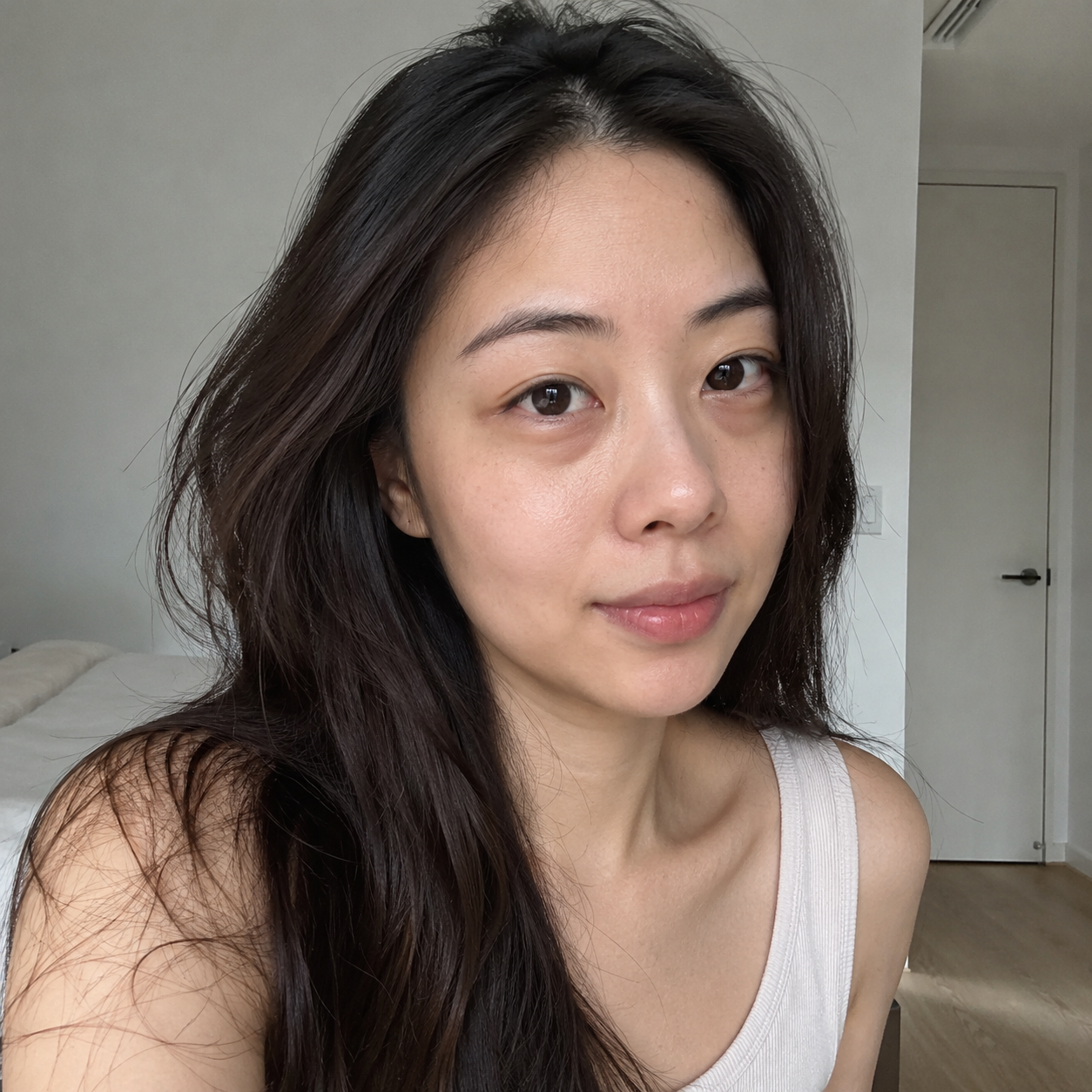 Young Asian woman with naturally fuller under-eye contours and a neutral facial expression.