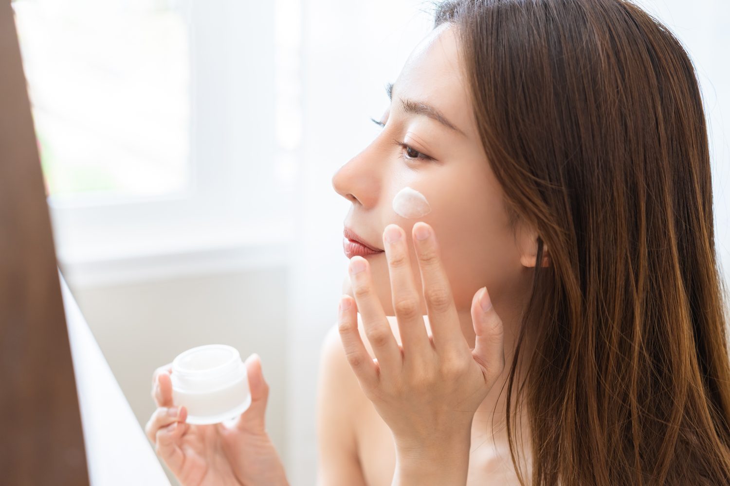 Woman applying moisturiser as part of skincare after treatment