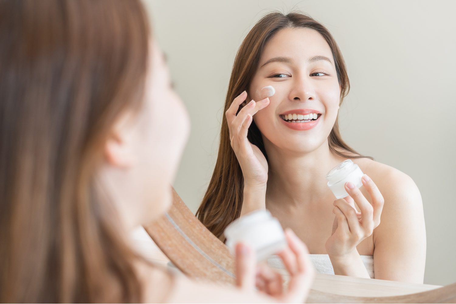 Woman applying moisturiser to her face in a mirror