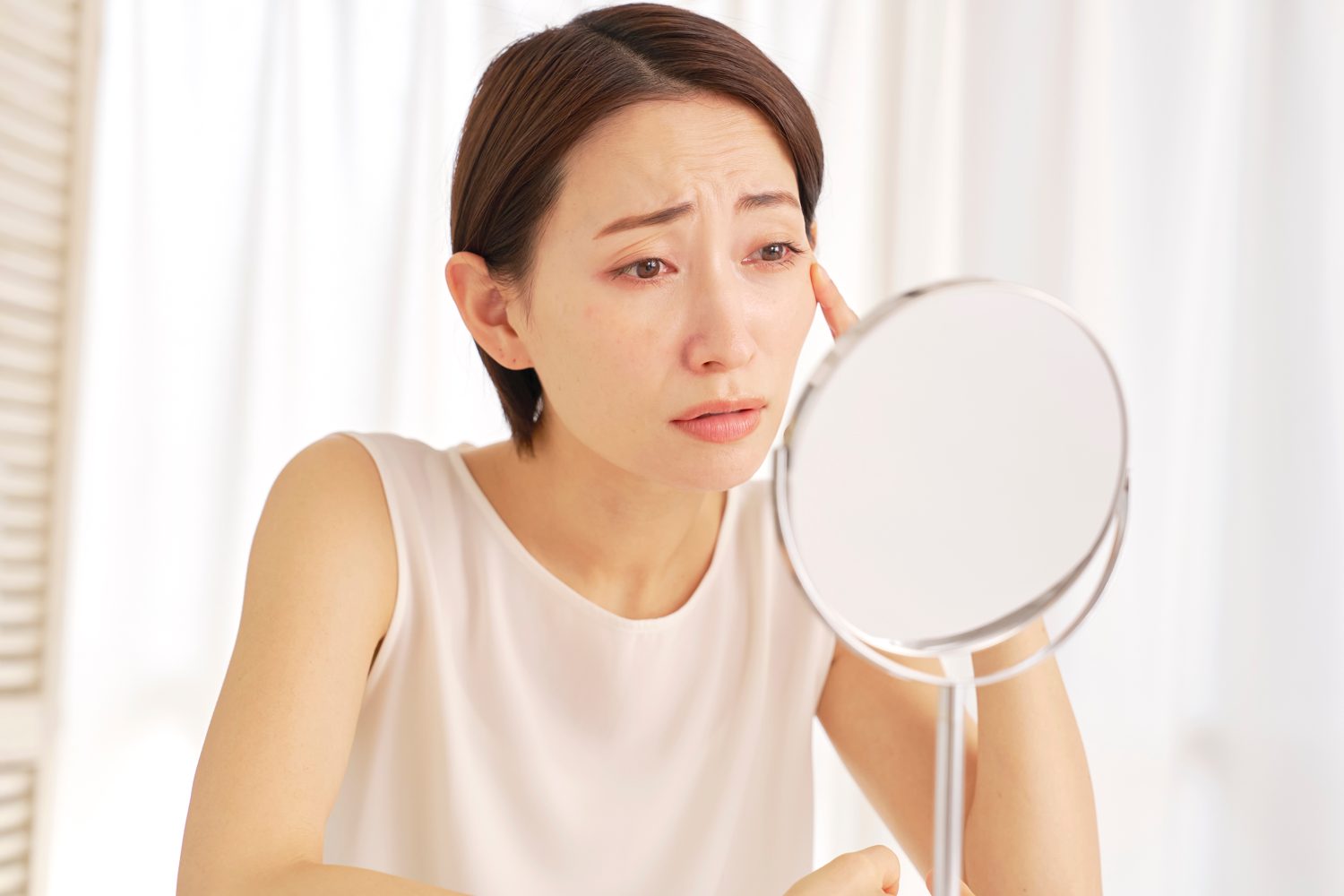 Woman examining fine lines around her eyes in a mirror